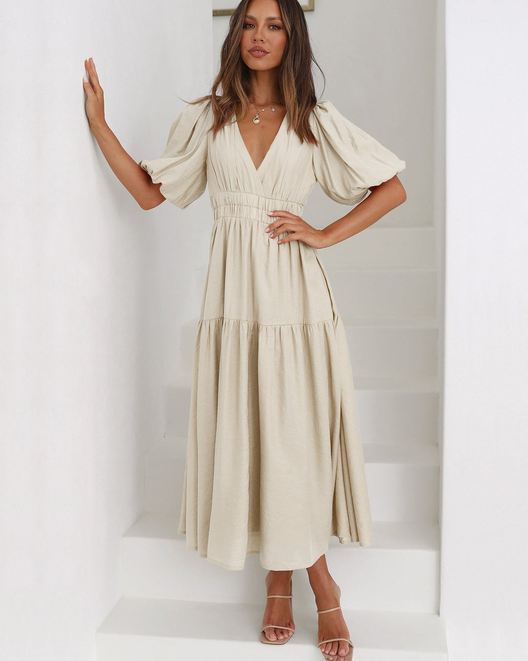 Woman walking in a chic smocked V-neck cocktail midi dress, perfect for spring/summer style & events.