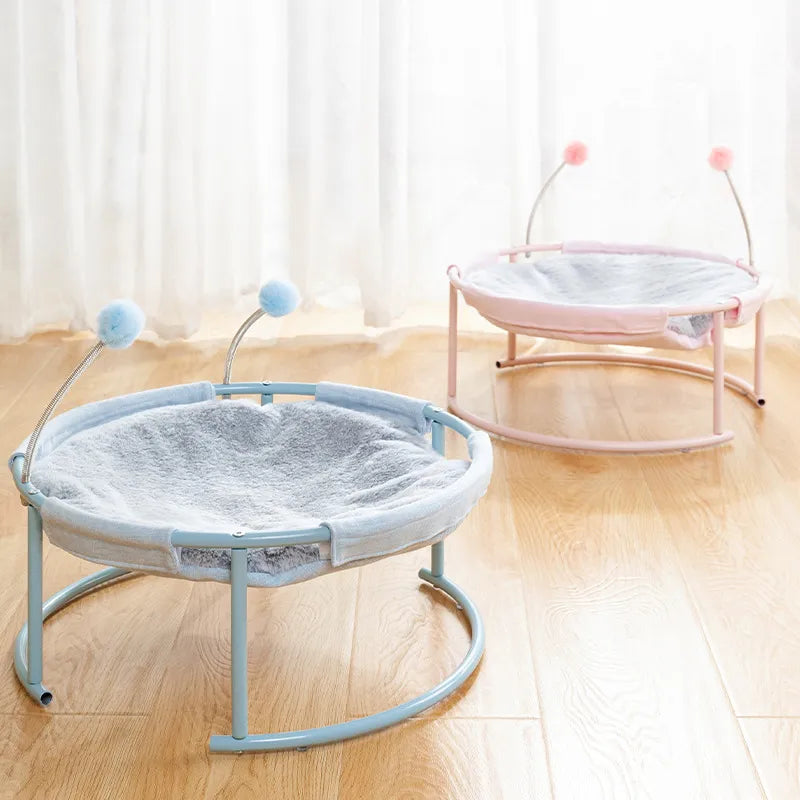 Happy cat napping in a plush round cat hammock, featuring a sturdy frame & fun dangling play balls.