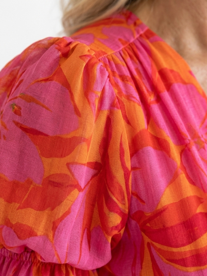 Close-up of women's floral V-neck midi dress, showcasing puff sleeves and delicate pink summer print.