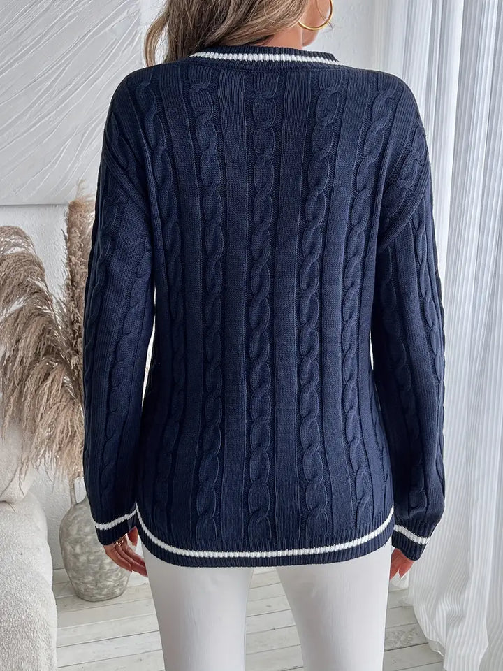 Intricate cable knit V-neck sweater for women in navy blue, accented with sophisticated striped trim. Warm & chic.