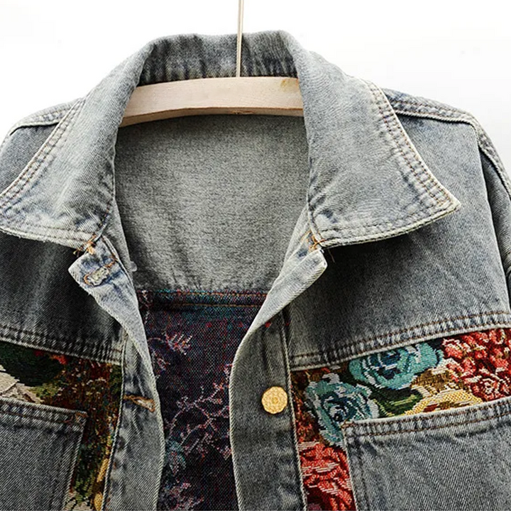 Women's denim jacket adorned with a vibrant, hand-painted floral print. Unique design for a fashion statement.