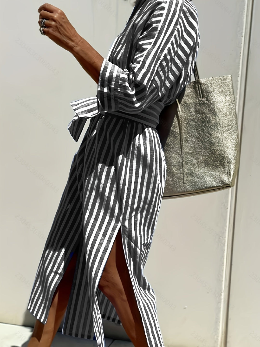 Full-length shot of a woman wearing a flowy striped button-down midi dress with a belt.
