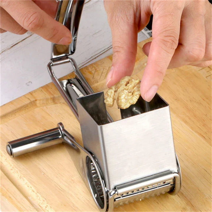 Hand-crank rotary cheese grater in action, shredding parmesan for cooking & serving. Stainless steel food prep tool.