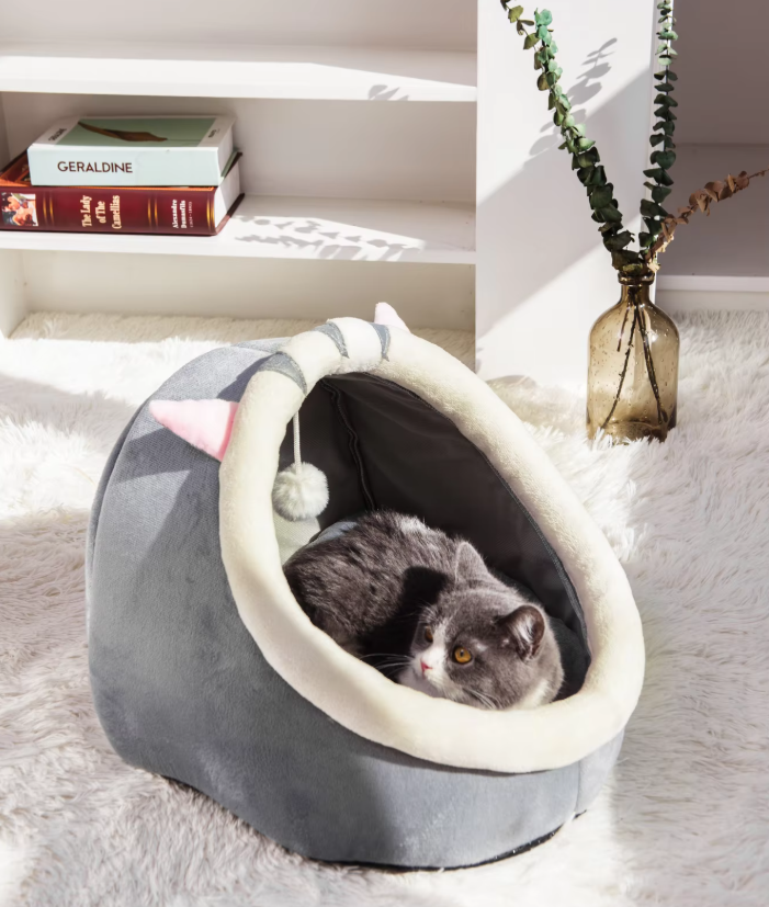 Soft plush unisex cat bed cave in an igloo design with playful ears & an attached ball toy. Cozy pet retreat.