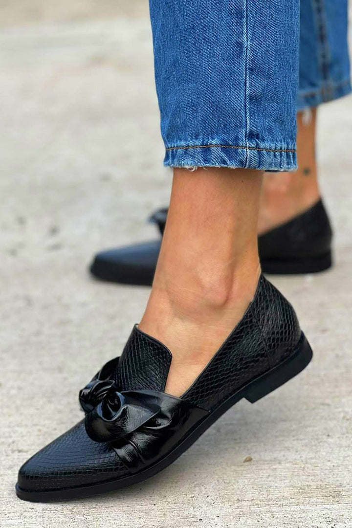 Classic black ladies' loafers showcasing an elegant bow detail, a comfortable and versatile slip-on shoe choice.