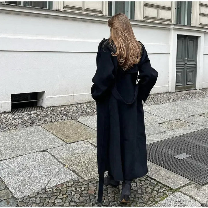 Woman models an elegant black double-breasted trench coat with a belted waist, ideal for chic fall fashion.