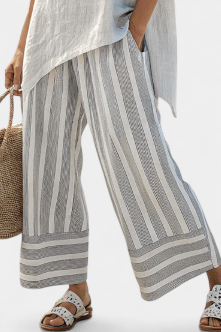Stylish women's asymmetrical blouse & multi-colored striped wide-leg pants set. Elegant casual two-piece outfit.