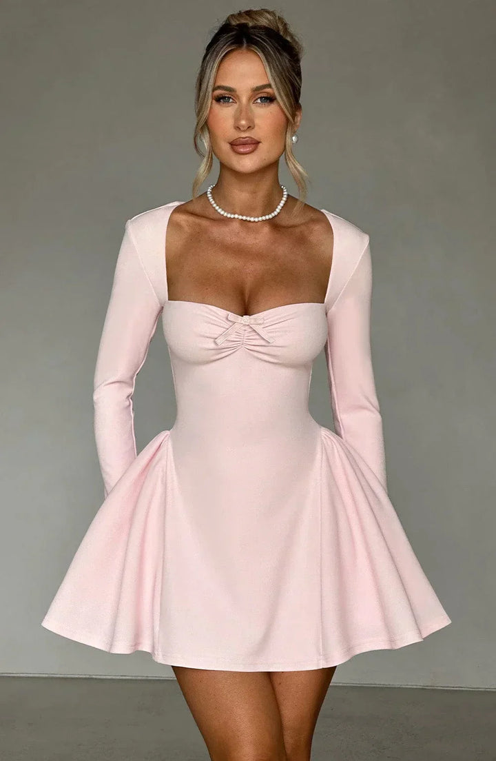 Woman models chic pleated A-line long sleeve mini dress. Elegant autumn party and occasion wear.