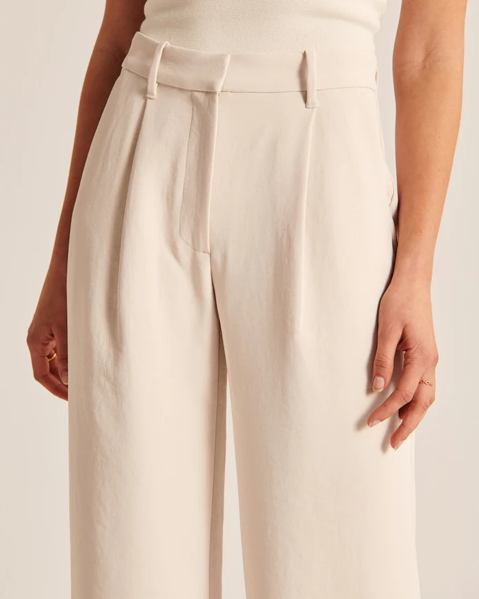 Model wearing women's beige wide-leg tailored trousers, high-waist, elegant style for both formal and casual occasions.