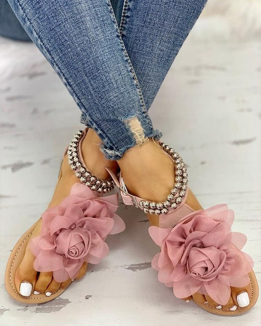 Close-up of elegant women's flat sandals showcasing delicate flower & pearl beaded straps for summer comfort.
