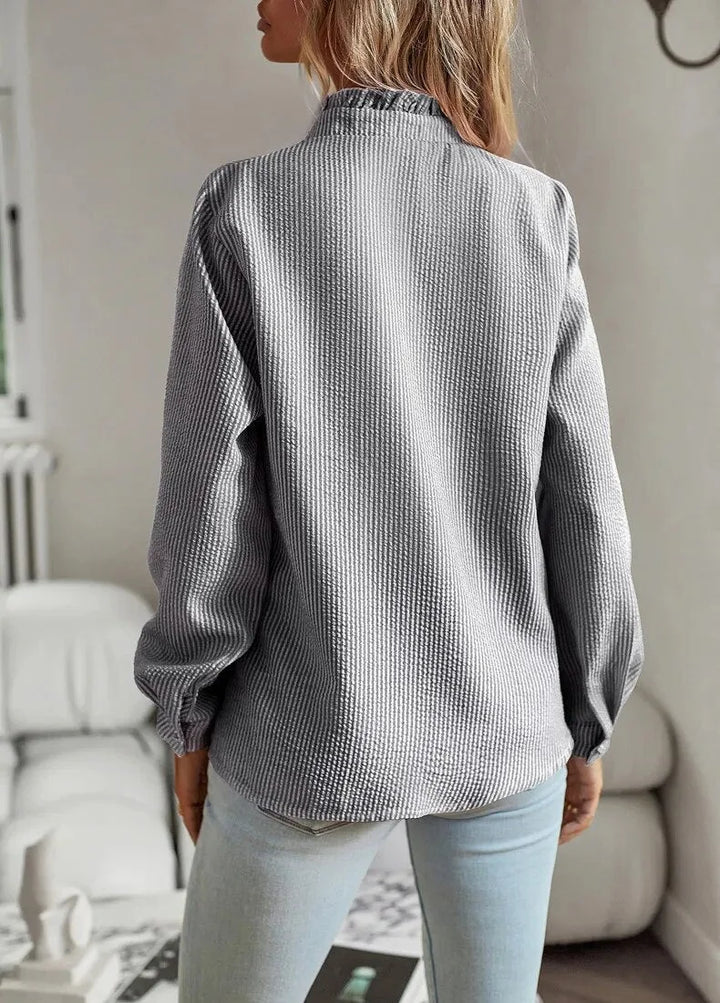 Woman modeling a pale blue textured striped blouse with a chic ruffled stand-collar and long sleeves.