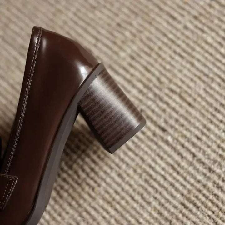Close-up of elegant tassels on women's brown loafer pumps. Features comfortable block heel & classic round toe footwear.