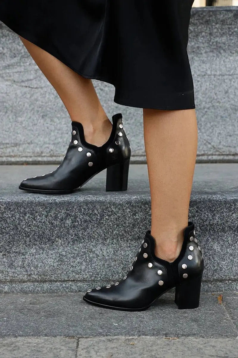 Close-up of women's edgy black studded ankle boots, featuring a stylish pointed toe and stable block heel.
