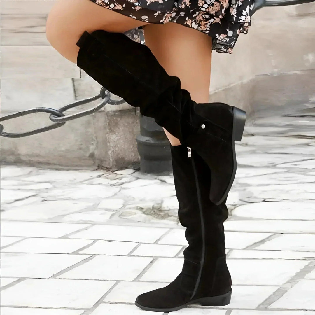 Pair of elegant women's slouchy pointed-toe knee-high boots, featuring prominent side zippers for easy entry.